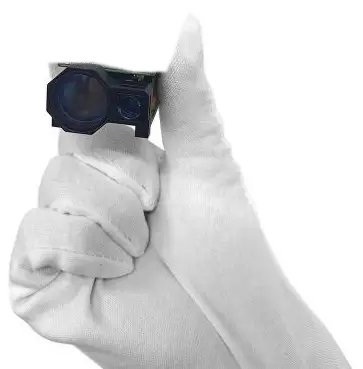 Gloved hand holding a compact laser rangefinder module